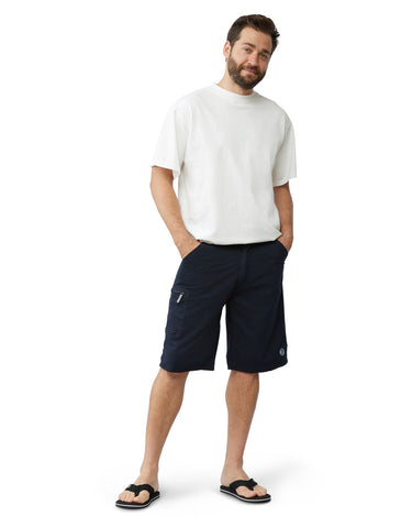Man with hands in pockets wearing black cotton cargo shorts and black flip flops with a white t shirt