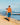 Man fishing on rocks with a fishing pole with black boardshorts on. Honolua bay in the background.