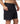 A close-up of a person wearing black 17" board shorts, showing the side pocket with a hand in the pocket.