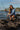 Woman crouching on rocks with fishing pole wearing sun shirt and boardshorts with large water bottle